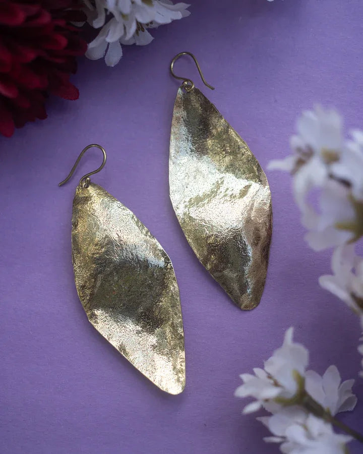 Long gold plated Fulani leaf drop earrings displayed on purple floral background.