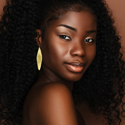 Model portrait wearing long gold plated Fulani leaf drop earrings highlighting bold ethnic design.
