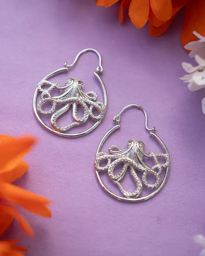 Silver and gold octopus drop earrings placed on purple floral background.