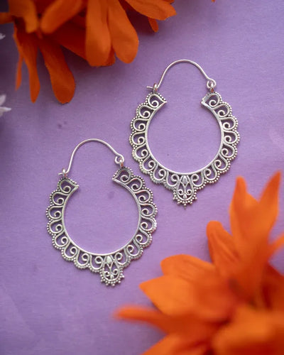 Flatlay of silver floral hoop earrings on purple background with flower decorations.