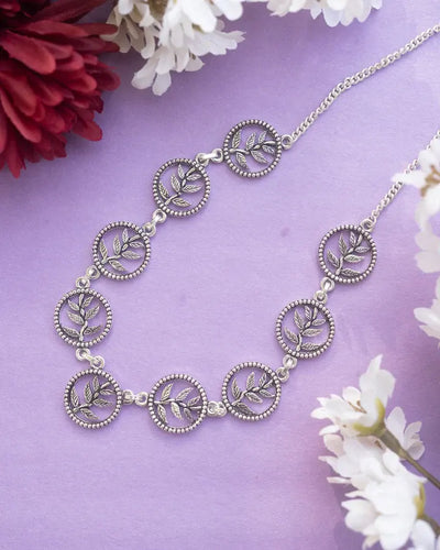 Silver round leaves choker chain necklace displayed on purple background with floral accents.