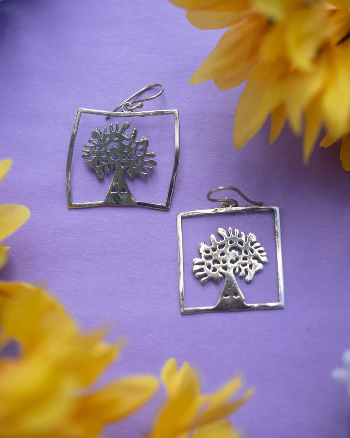 Tree of life square gold dangling fish hook earrings displayed on purple background with flowers.