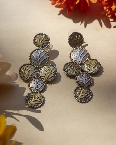 Two Tone Gold and Silver Leaf Dangle Drop Earrings displayed with flowers and warm lighting.