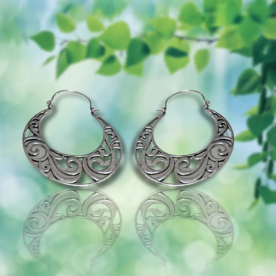 Vintage curvy silver boho hoop earrings showcased on a green leaf background.