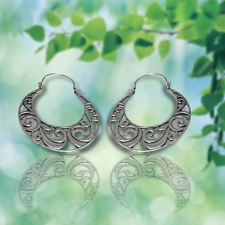 Vintage curvy silver boho hoop earrings showcased on a green leaf background.