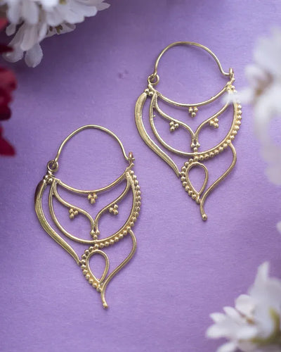 Pair of asymmetrical antique gold plated hoops earrings displayed on purple background.