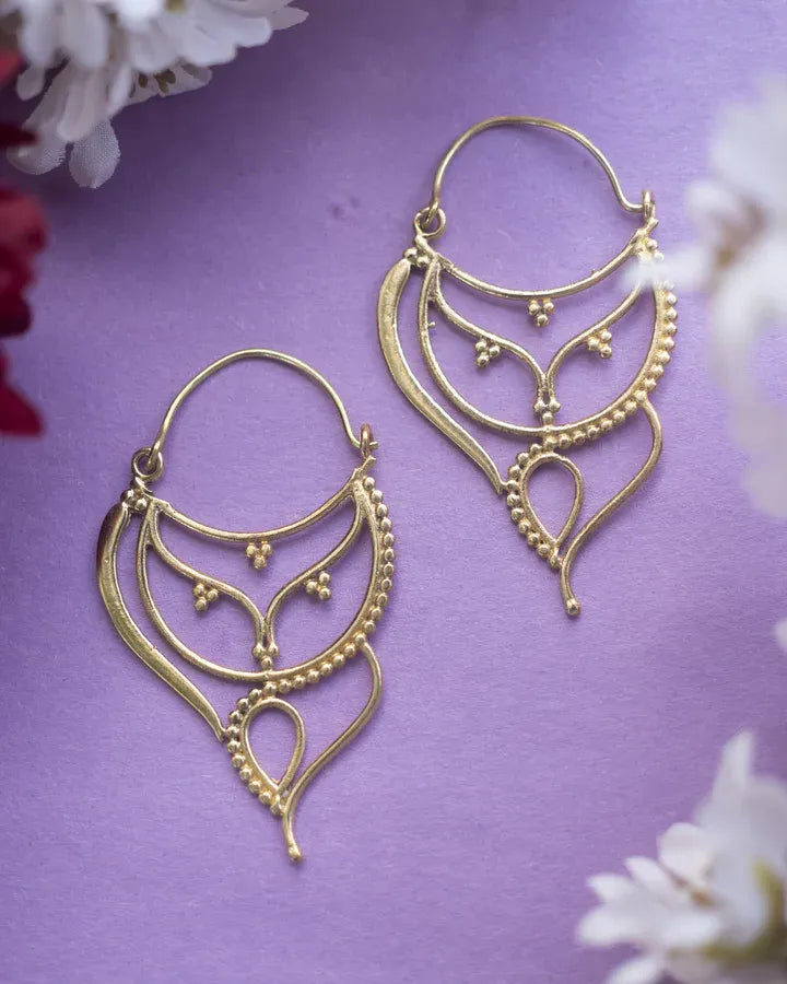 Pair of asymmetrical antique gold plated hoops earrings displayed on purple background.